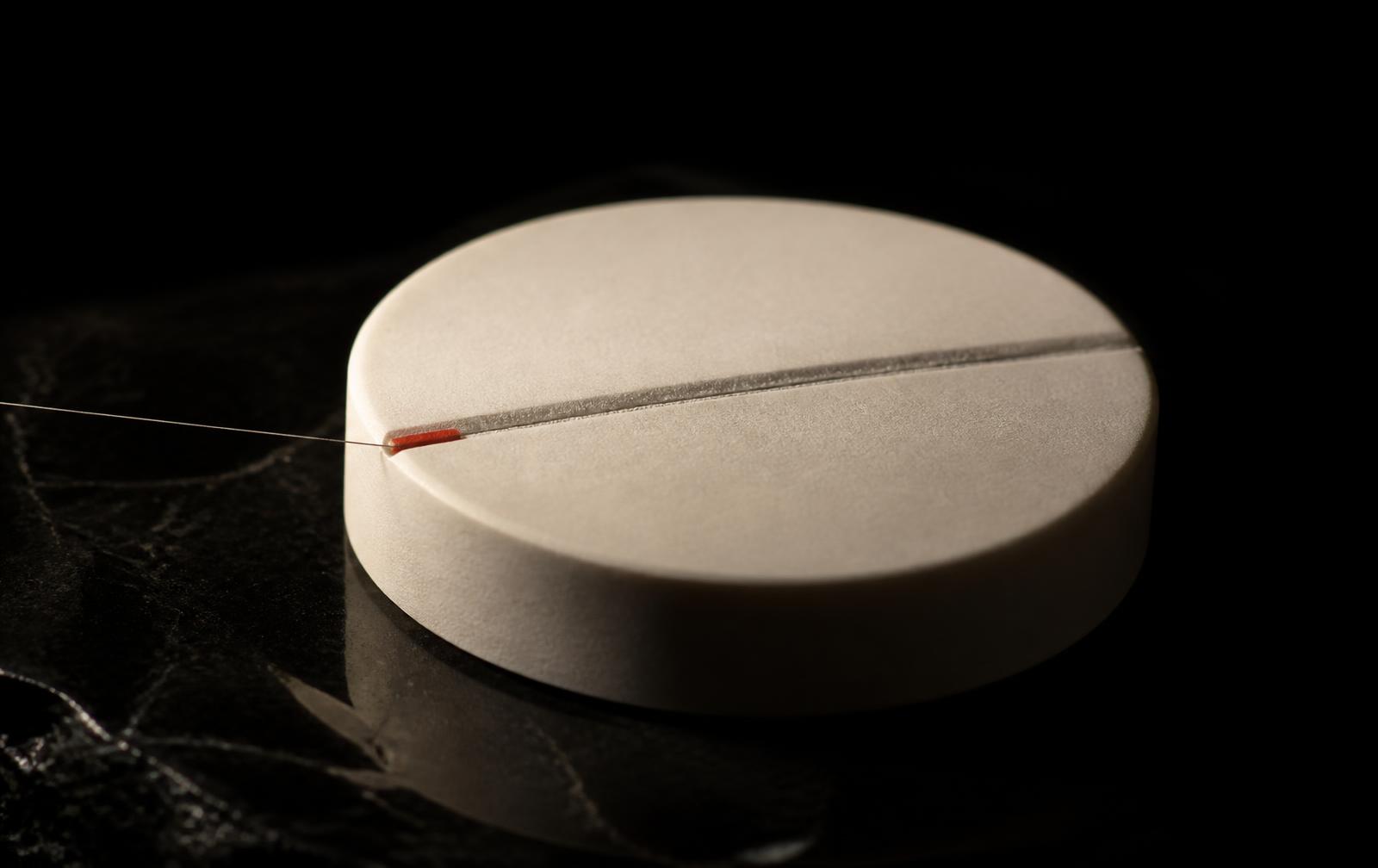 A machined bone-white disc on black glass with an oxide-red index mark against a steel hairline